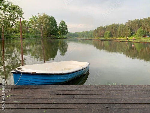 Wooden boat on the pier on the background of the lake. Fishing boat on the shore of a forest reservoir. The boat is tied to the shore. Concept: outdoor recreation, tranquility by the water.