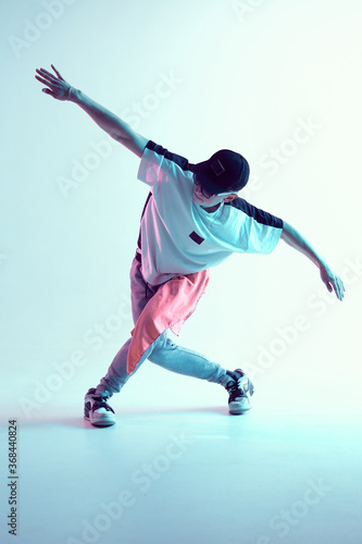 Guy dancing contemporary dance in studio. Neon light blue background. Acrobatic bboy dancer. Break dance lessons. photo