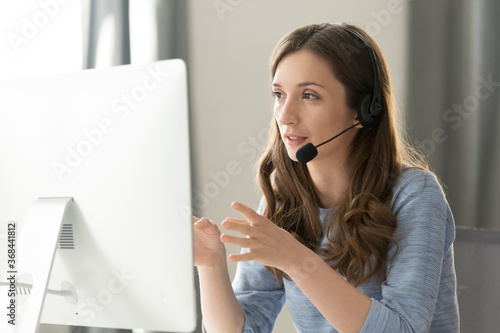 Serious call center operator in wireless headset talking with customer, woman in headphones with microphone consulting client on phone in customer support service, looking at computer screen close up photo