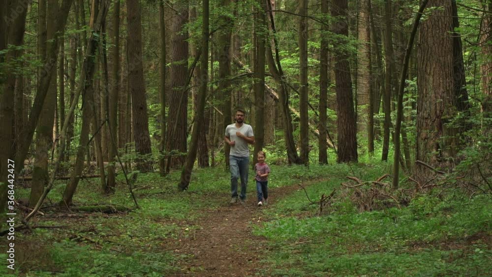 Happy family, young father and little child girl run along forest path in large summer coniferous forest. Outdoors. Nature sports and leisure concept Happy family, young father and little child girl run along forest path in large summer coniferous forest. Outdoors. Nature sports and leisure concept