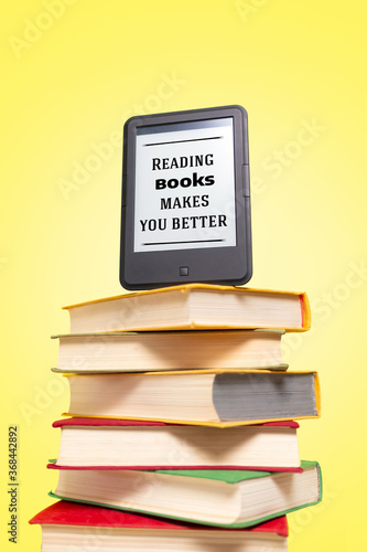 Reading. E-book on top of a stack of books on a yellow background. Vertical. Concept of education and electronic gadgets