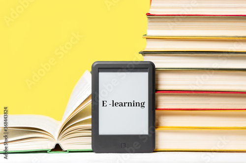 E-learning. E-book reader and a stack of books on a yellow background. Concept of education and electronic gadgets