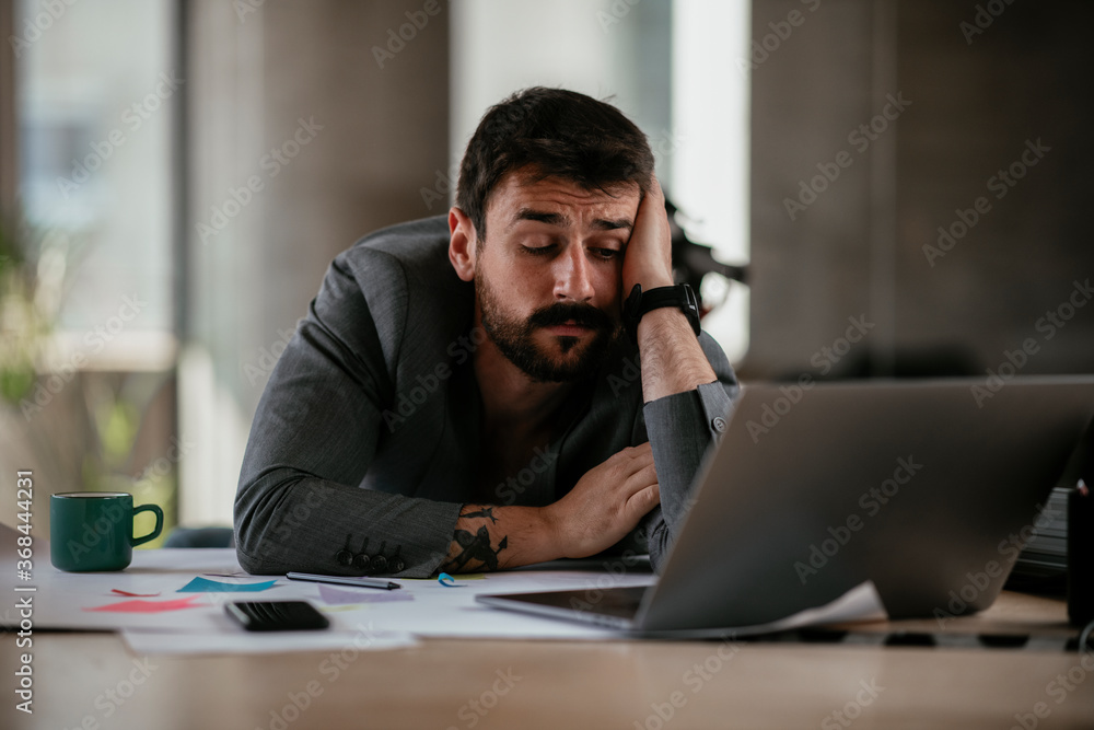 Tired businessman working with laptop at office. Businessman sitting at office desk working on laptop computer.. Tired businessman working with laptop at office. Businessman sitting at office desk working on laptop computer..