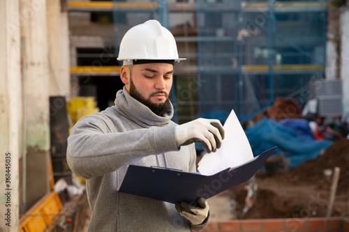 Young bearded foreman making task list during works in building under construction