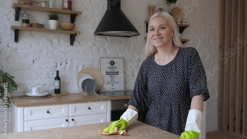 Young housewife wear rubber protective gloves cleans wooden surface and smile 4K photo