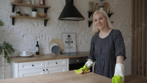 Young housewife wear rubber protective gloves cleans wooden surface and smile 4K photo