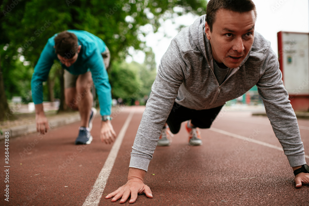 Young men exercising on a race track. Two young friends training outdoors.. Young men exercising on a race track. Two young friends training outdoors..