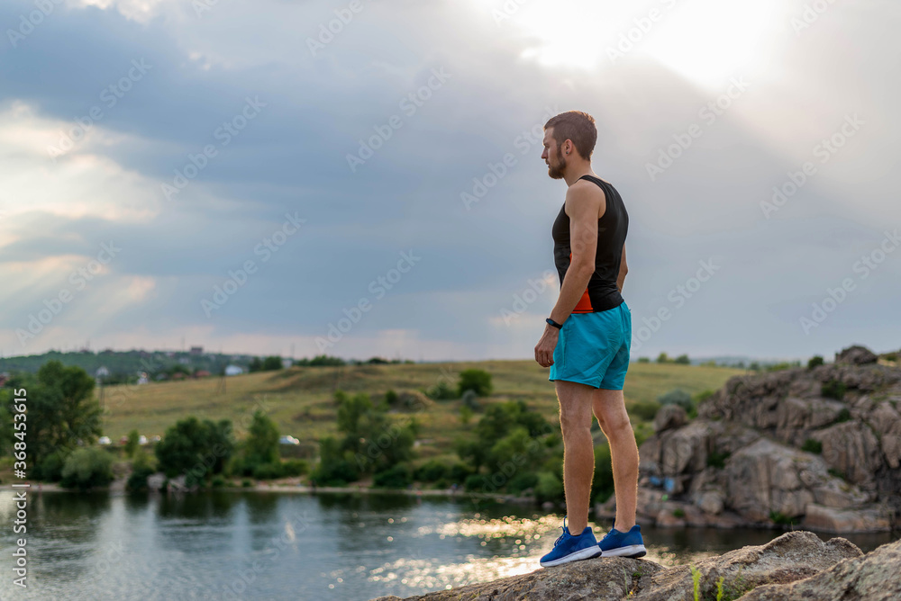 A male runner stands at the edge of a cliff and looks out at the river. A male runner stands at the edge of a cliff and looks out at the river.
