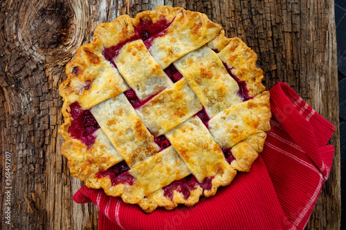A fresh baked strawberry rhubarb pie with overlay crust on a barn plank wood table ready to slice and eat for a favorite dessert in Michigan, USA.
