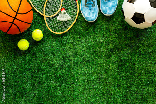 Sport games equipment - balls, sneakers, rackets - on grass top view copy space