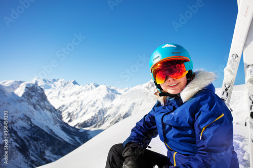 Happy portrait of a teen girl in ski helmet and put down mask smile over mountain summit peaks