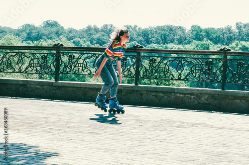 Very beautiful teenager girl rides on roller skates in a summer park in the city