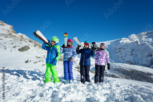 Boy with ski sport equipment on shoulder stand in a group of friends over mountain peak on background