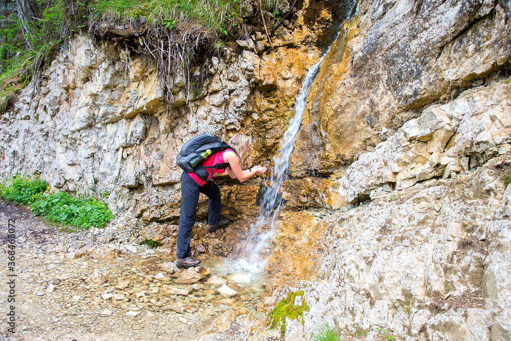 Adult hiker drinks water at the spring in Dolomites, Lago Sorapis, Italy