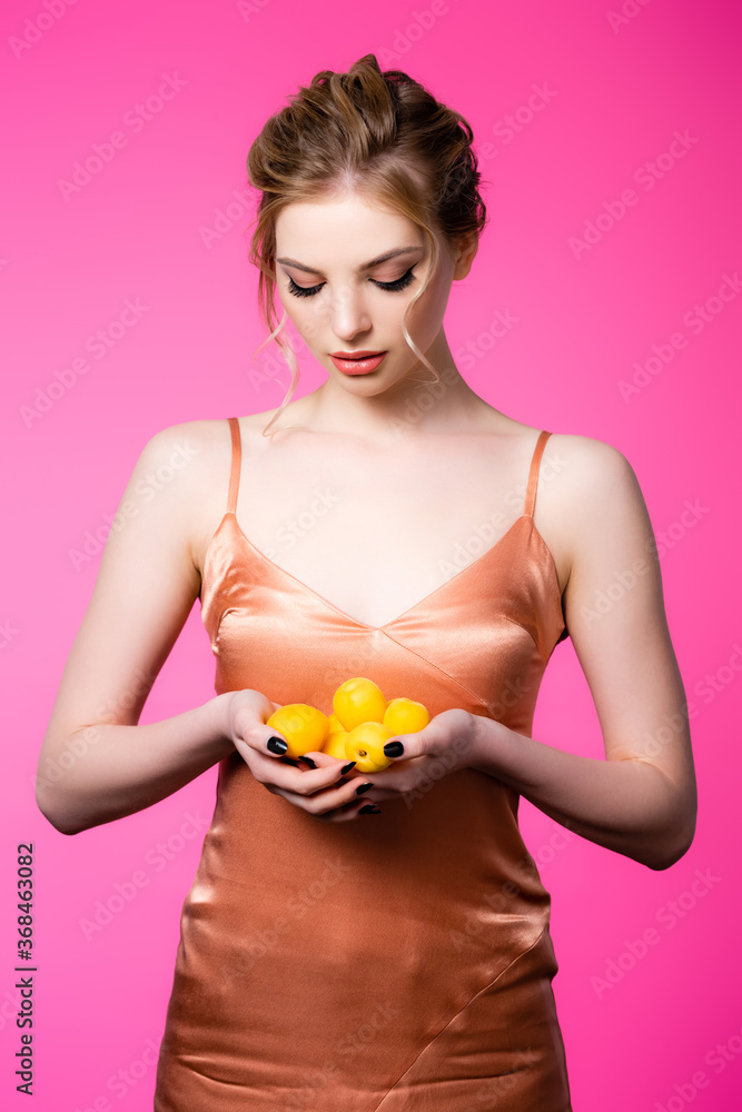 elegant beautiful blonde woman in silk dress looking at ripe apricots isolated on pink elegant beautiful blonde woman in silk dress looking at ripe apricots isolated on pink