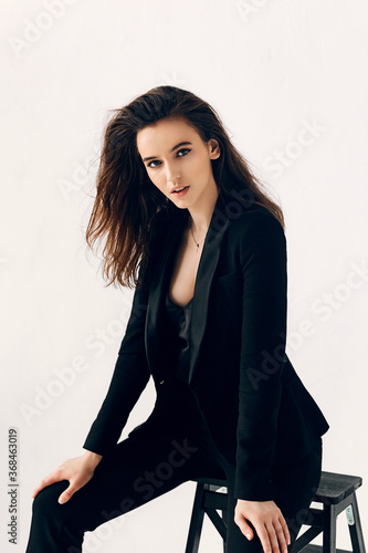Close up portrait of young cheerful beautiful woman with dark long hair in black suit.