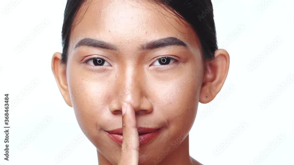 Portrait of Asian woman giving a shushing gesture raising her finger to her lips as she asks for silence Portrait of Asian woman giving a shushing gesture raising her finger to her lips as she asks for silence