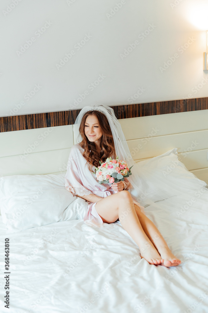 Morning of the bride in a pink robe and a veil in the hotel on the bed, wedding dress Morning of the bride in a pink robe and a veil in the hotel on the bed, wedding dress