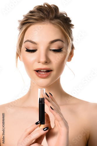naked beautiful blonde woman with makeup and black nails looking at stick concealer isolated on white
