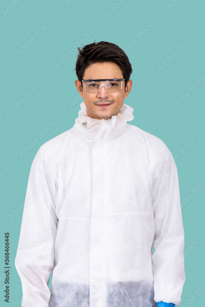 Portrait of confident male Asian researcher scientist medical doctor wearing Personal Protective Equipment (PPE), surgical mask, and protection glasses; standing isolated on light green background Portrait of confident male Asian researcher scientist medical doctor wearing Personal Protective Equipment (PPE), surgical mask, and protection glasses; standing isolated on light green background