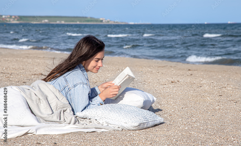 A young woman lies by the sea on the beach and reads a book