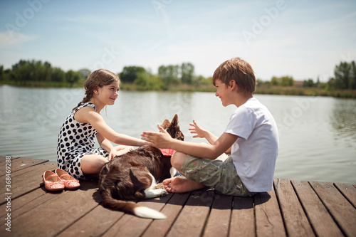 Brother and sister enjoying on the dock of the lake with their dog