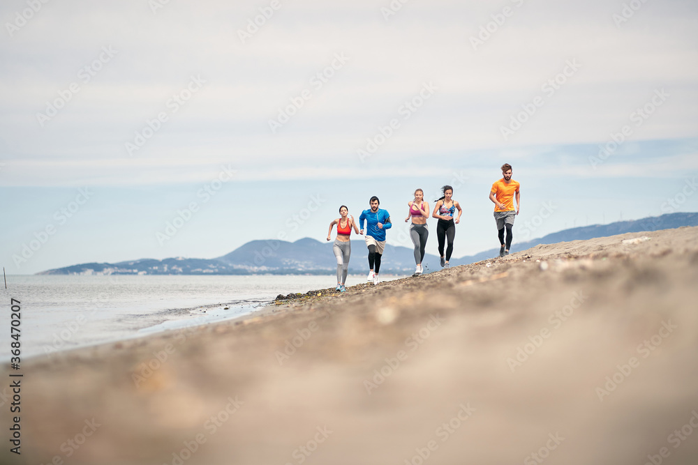 Group of young friends running and exercising on the beach.