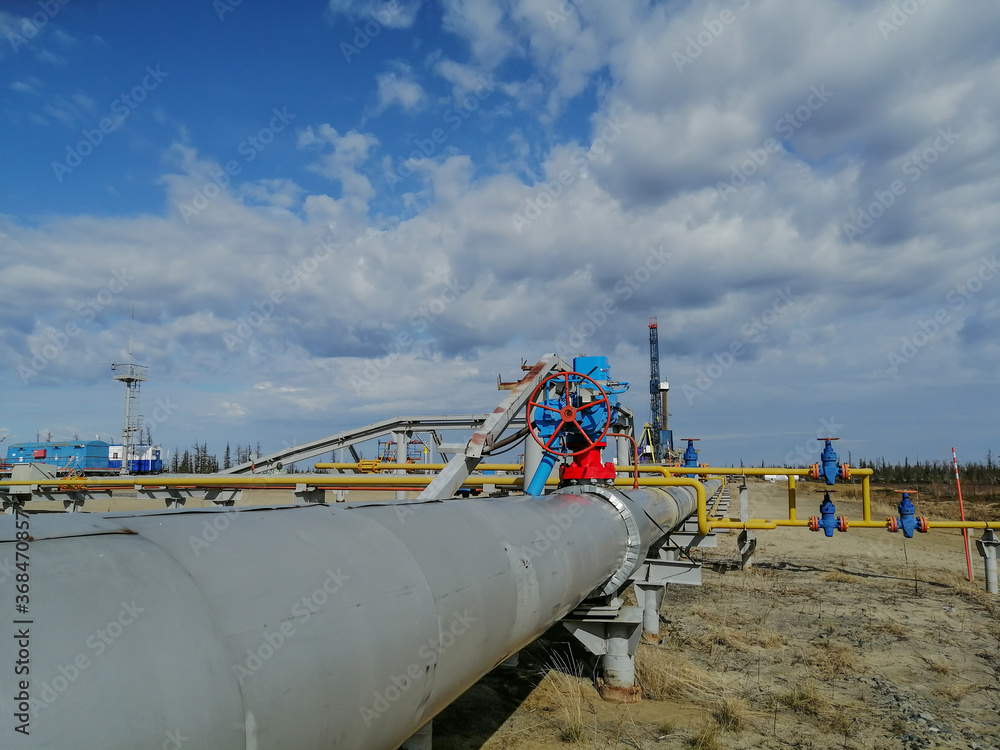 Pipeline fittings and manifold of producing gas wells in the field. Handwheels for high pressure valves. In the background, a drilling rig. Blurring distant objects.