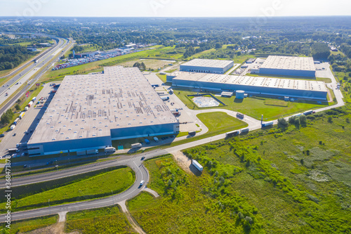 Aerial Top View of Industrial Storage Building Area with Solar Panels on the Roof and Many Trucks Unloading Merchandise.