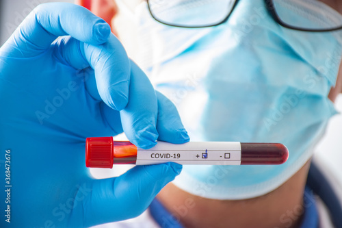Laboratory technician, medical specialist, doctor or scientist holds blood test tube in his hand, where coVID-19 is written and positive result of analysis for coronavirus is shown to camera close-up