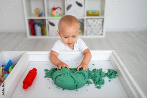 Baby playing with green kinetic sand and rolling pin. Little girl playing with sand at home, games, education, children room