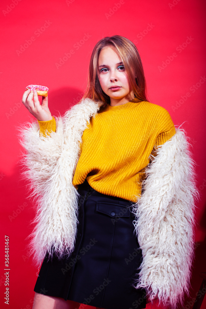 young pretty fashion teenage girl on bright red background holding donut, happy smiling lifestyle people concept young pretty fashion teenage girl on bright red background holding donut, happy smiling lifestyle people concept