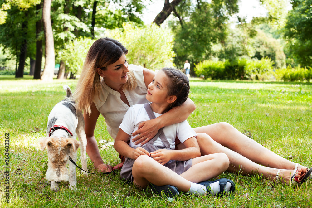 young pretty caucasian mother walking with little cute daughter and dog fox terrier, lifestyle people concept