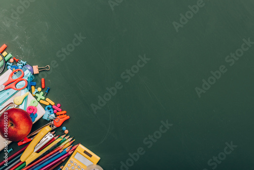 top view of delicious apple, calculator and school supplies on green chalkboard with copy space