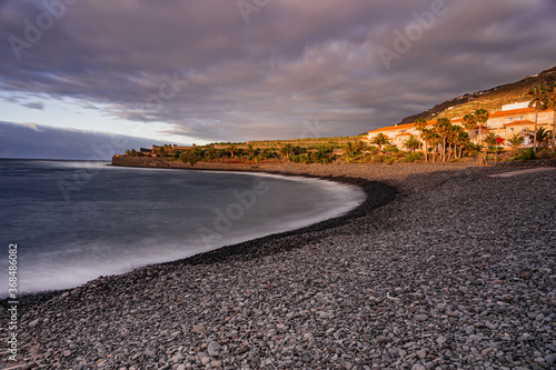La Caleta of Interian pebbles beach, with sunset sunlight and grey clouds, long exposure, Tenerife, Canary islands, Spain photo