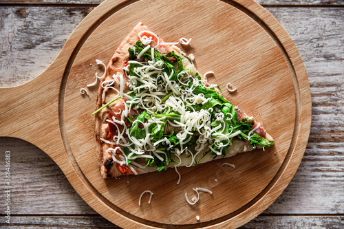 Top down view of fresh pizza slice with prosciutto, rocket salad and cheese on wooden board.
