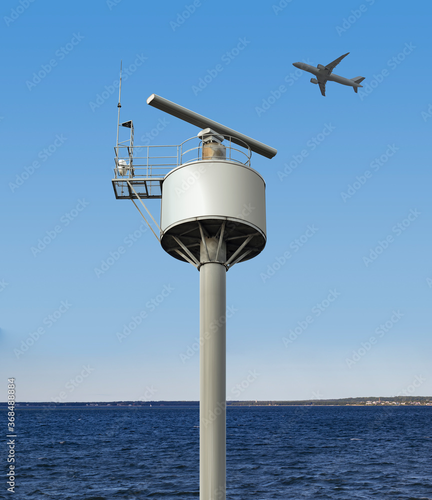 Rotating coastal radar surveillance station under the clear summer sky by the sea catching an airplane flying in the air space