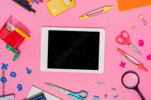 Top view of digital tablet with blank screen near school stationery on pink