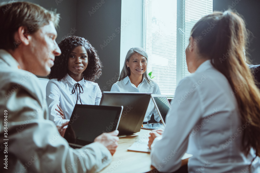 Funny business meeting of diverse team. Happy Multiethnic group of people have conversation sitting at office desk and using computers. Tinted image. Funny business meeting of diverse team. Happy Multiethnic group of people have conversation sitting at office desk and using computers. Tinted image.