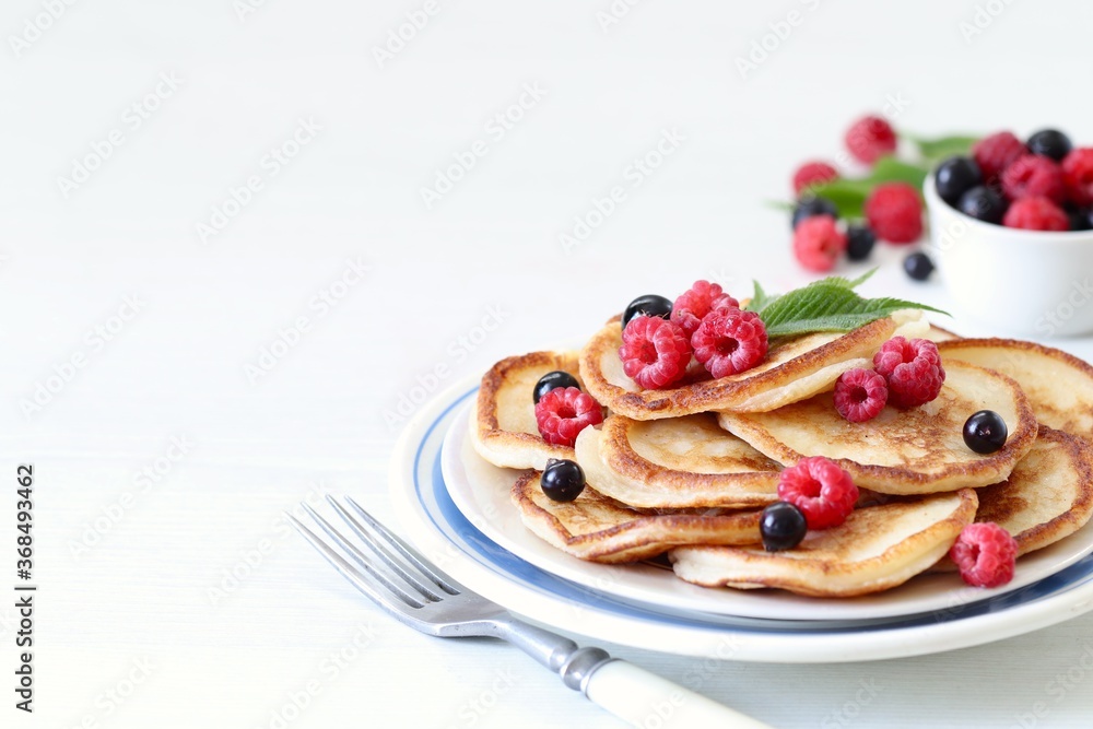 Pancakes with fresh raspberries and black currant on a plate on a white background copy space 