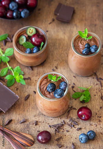 Fototapeta Naklejka Na Ścianę i Meble -  Portion jars with chocolate mousse or pudding decorated with sweet cherry, blueberry and mint and pieces of chocolate. Selective focus. Rustic style. Dark background.