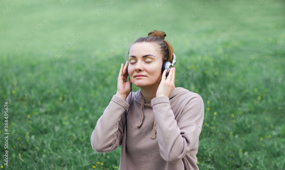 Pretty young girl smiling with pleasure as she listens to music with her eyes closed in bliss while lying on her stomach on the grass in a green lush garden enjoying the spring sunshine Pretty young girl smiling with pleasure as she listens to music with her eyes closed in bliss while lying on her stomach on the grass in a green lush garden enjoying the spring sunshine
