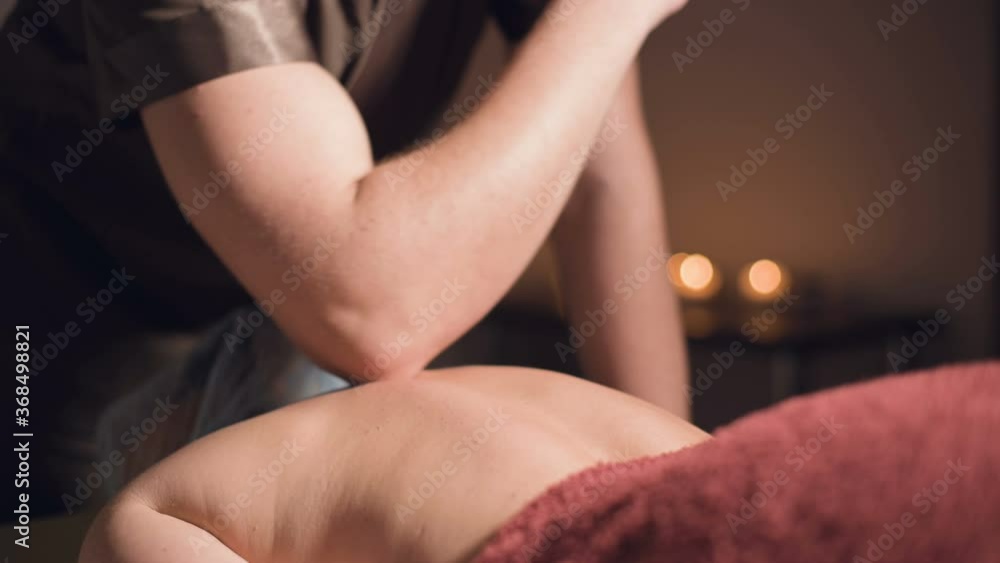 A young male masseur does a professional massage with an elbow to a client girl in a professional massage parlor with lit candles in a dark room A young male masseur does a professional massage with an elbow to a client girl in a professional massage parlor with lit candles in a dark room