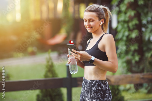 Young woman checking smart phone after workout on the green park background.