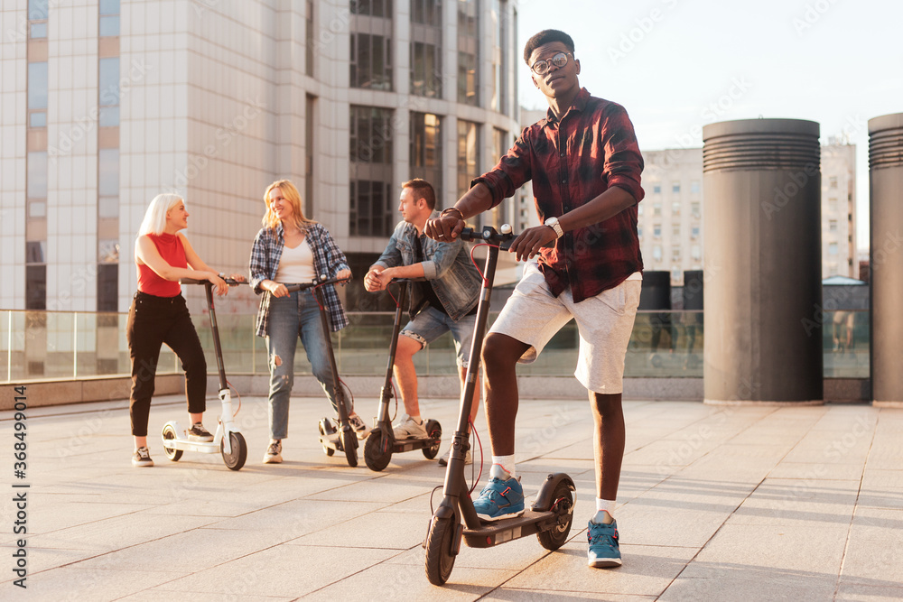 portrait of an African American guy in a European group of friends, people use electric scooters and communicate