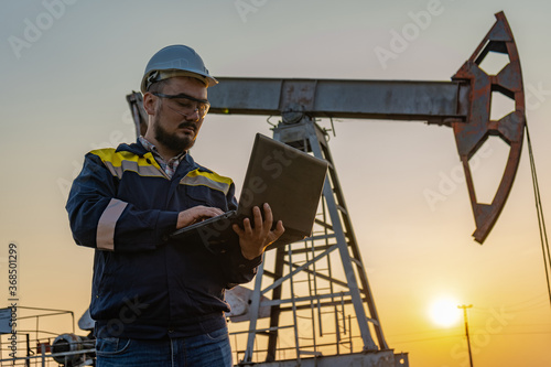 Engineer with a laptop against the background of oil rockers.