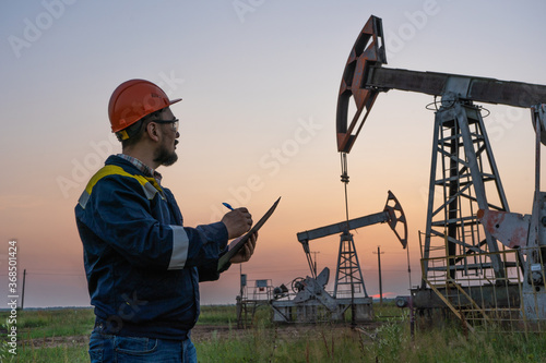 Oil worker checks an oil rig at sunset. Maintenance of oil pump jacks