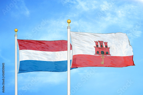 Netherlands and Gibraltar two flags on flagpoles and blue sky photo