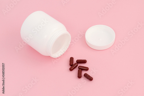 Brown pills near a white jar on a pink background. Concept boost immune system, medicine and tablets.