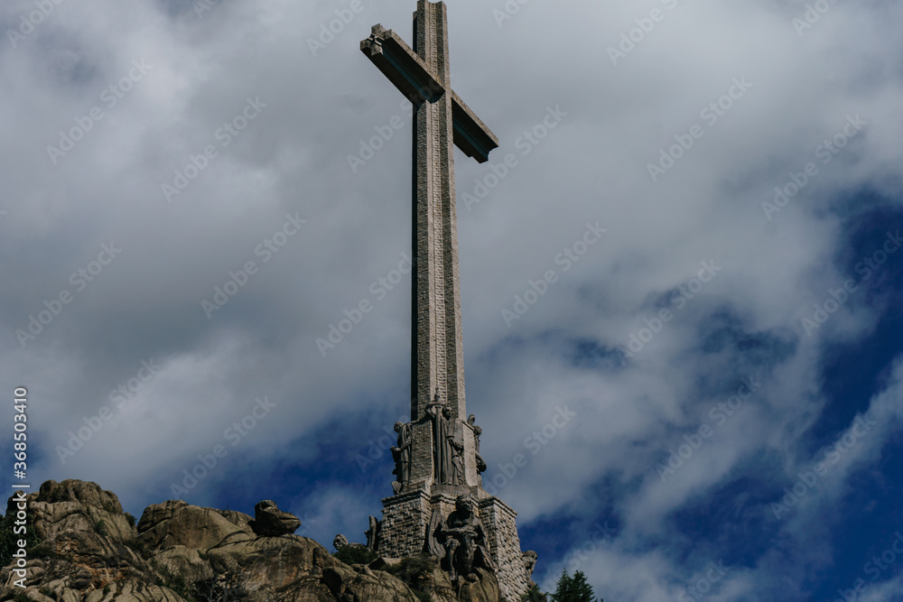 Cross on the top of the Valley of the Fallen in Madrid with white clouds in a very blue sky. The cross is settled on a rock hill Cross on the top of the Valley of the Fallen in Madrid with white clouds in a very blue sky. The cross is settled on a rock hill